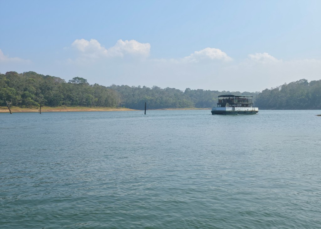 Tour boat on a wide lake with forested hills in the background under a pale blue sky.