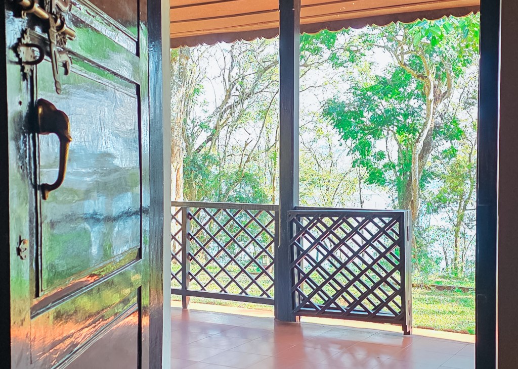 View from inside a doorway onto a veranda with wooden lattice railings overlooking trees and water.